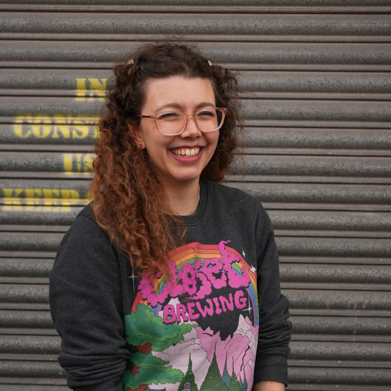 Person wearing a colorful t-shirt with text and graphics, standing in front of a corrugated metal wall.