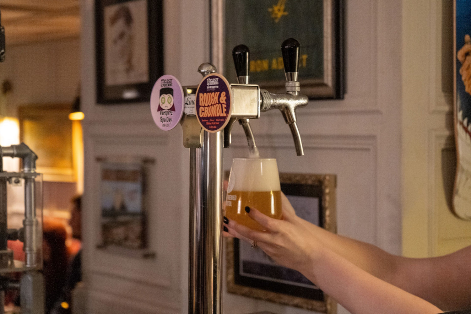 two beer taps displaying badges of two different beers, while hands hold a full glass of beer beside them